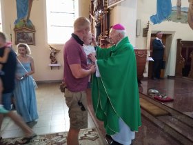 Ksiądz arcybiskup Edmund Piszcz błogosławi dziecko na rękach ojca
